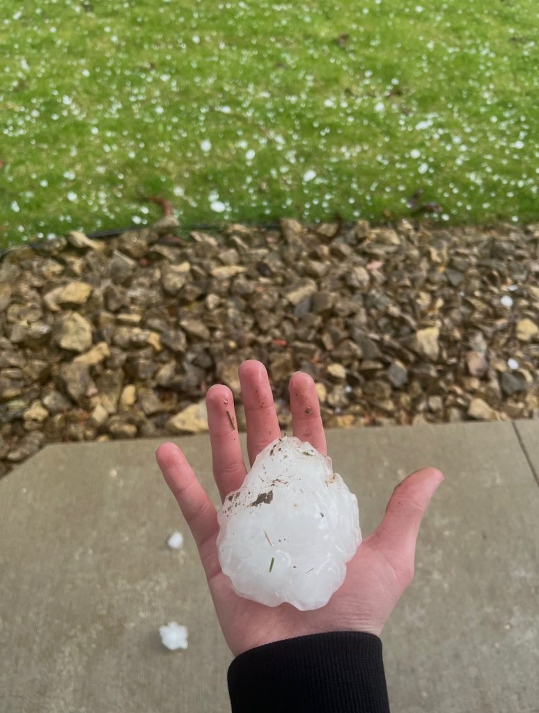 A hand holding a bal of hail that is almost as big as the palm. 